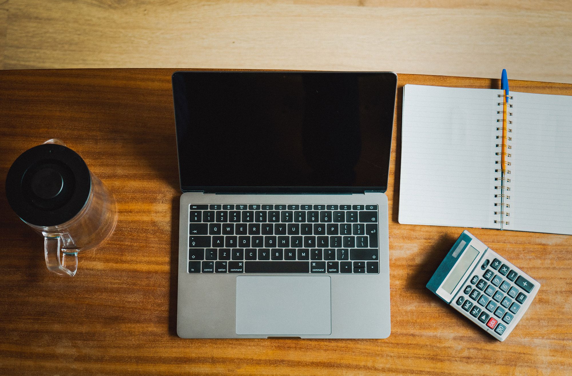 Laptop, calculator, notebook, and pen arranged on a bookkeeping desk